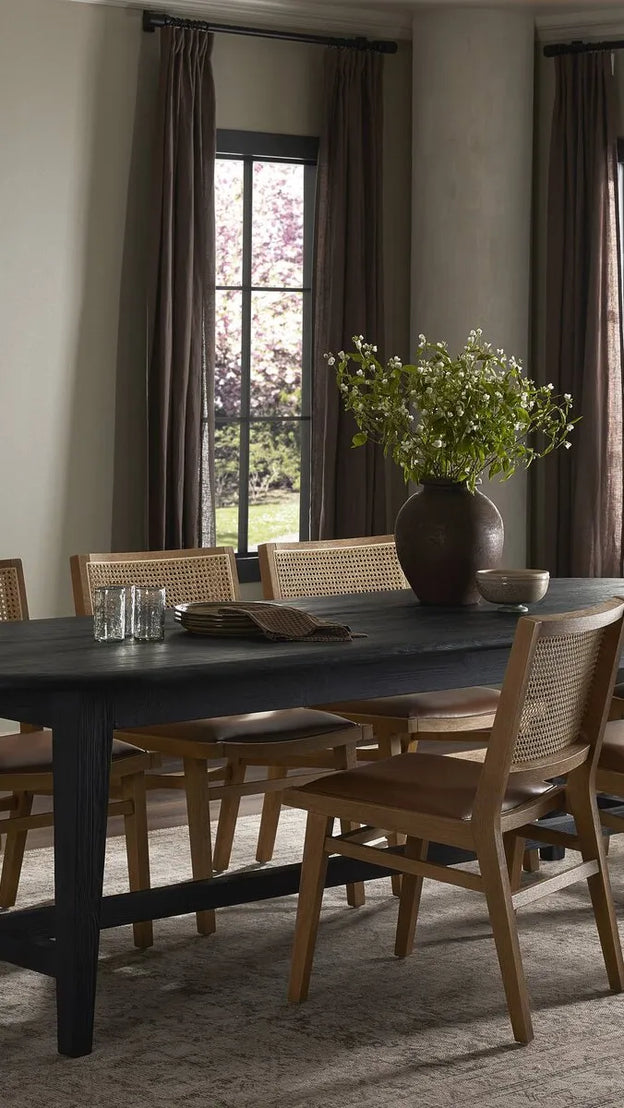 Salle à manger chaleureuse avec grande table noire, chaises en bois et arrangement floral