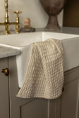 Linge à vaisselle gaufré beige suspendu à un évier en porcelaine