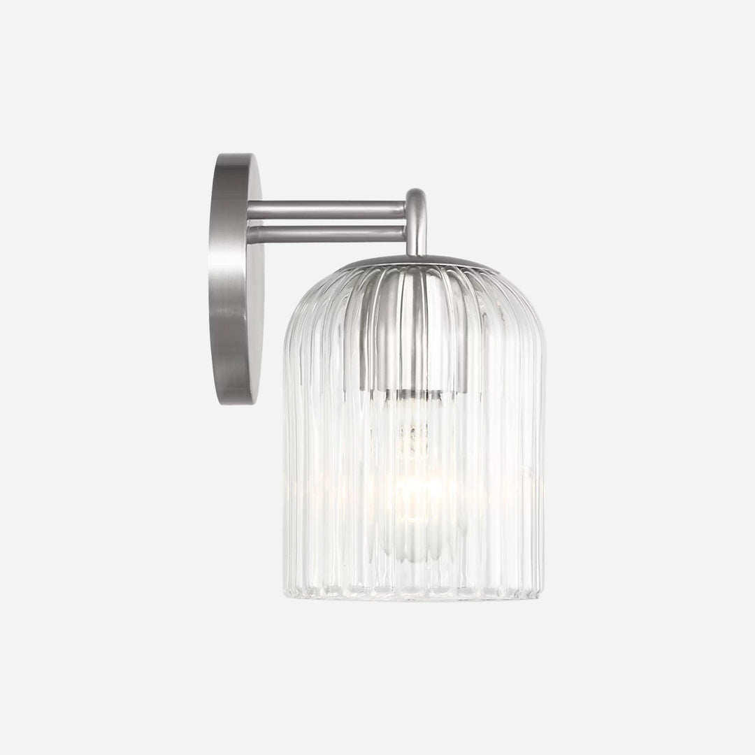 Applique murale Maison Olive Eisele avec support en métal brossé et abat-jour cylindrique en verre strié transparent.