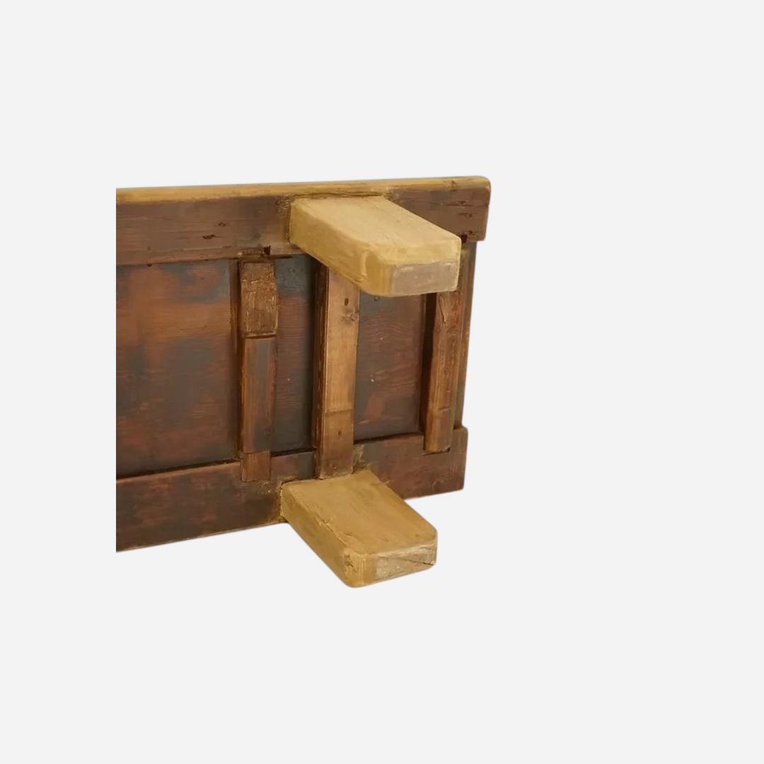 Vue de dessous d'un banc bas artisanal Maison Olive en bois massif sombre avec pieds robustes et structure apparente.