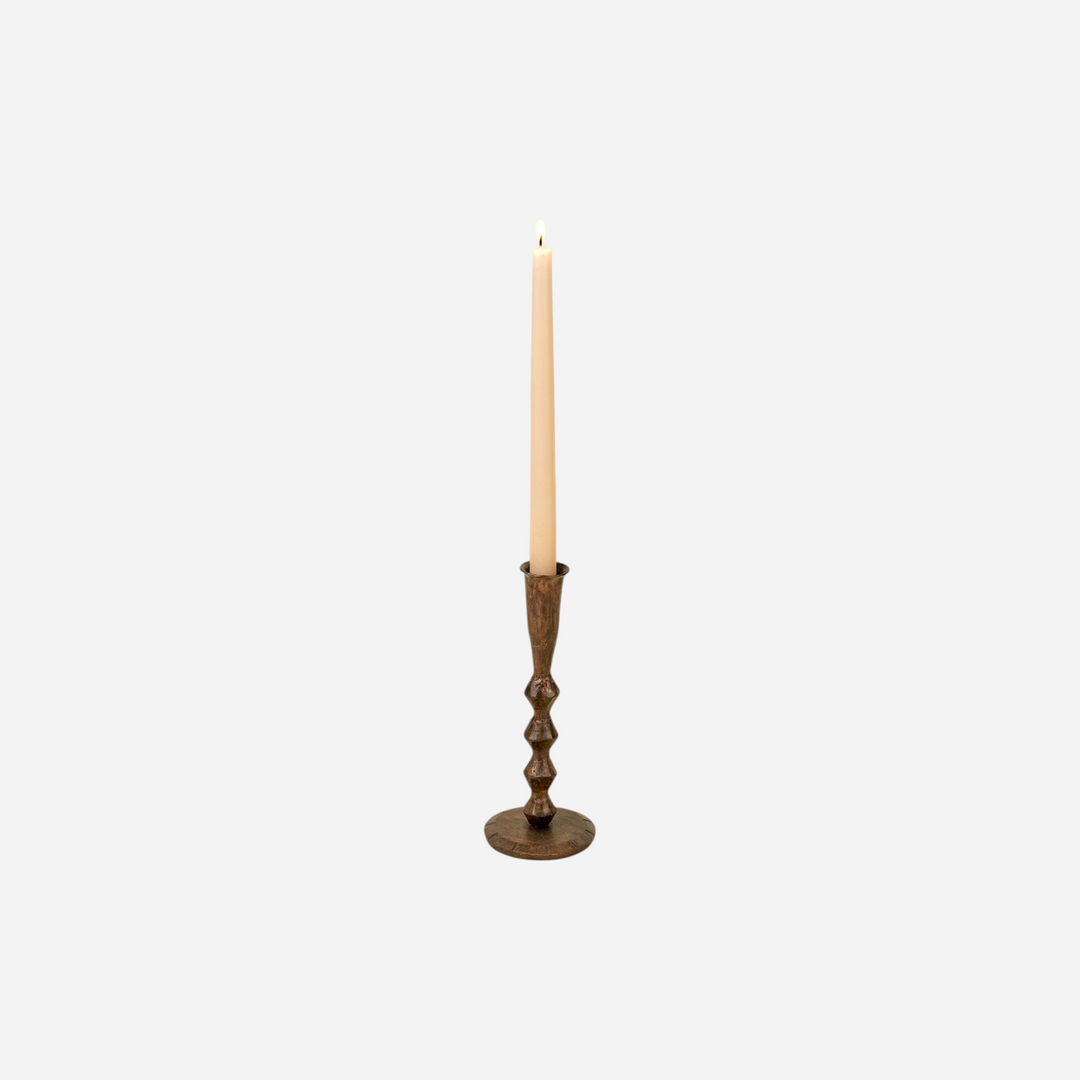 Bougeoir artisanal Maison Olive en métal patiné sombre avec une bougie effilée sur fond beige clair