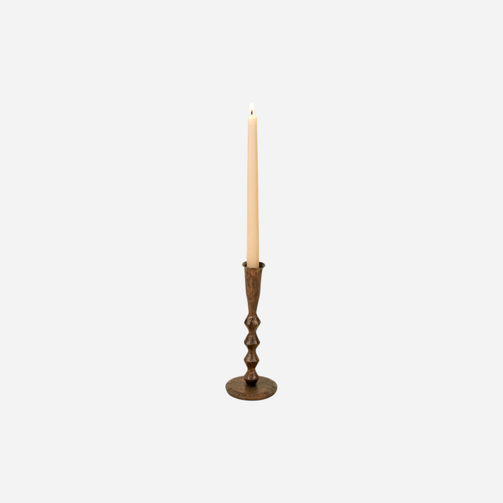 Bougeoir artisanal Maison Olive en métal patiné sombre avec une bougie effilée sur fond beige clair