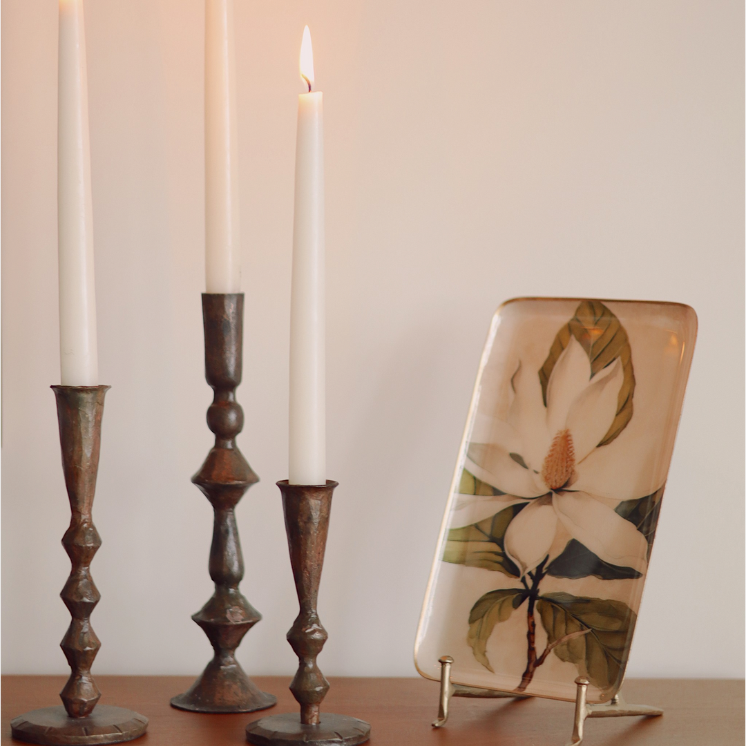 Trois bougeoirs Maison Olive en métal patiné de hauteurs variées avec des bougies blanches allumées sur une console
