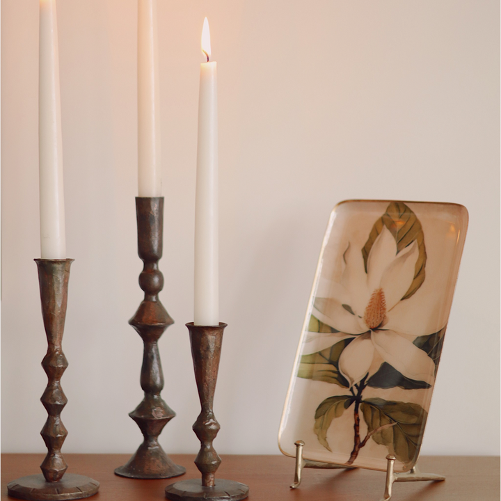 Trois bougeoirs Maison Olive en métal patiné de hauteurs variées avec des bougies blanches allumées sur une console