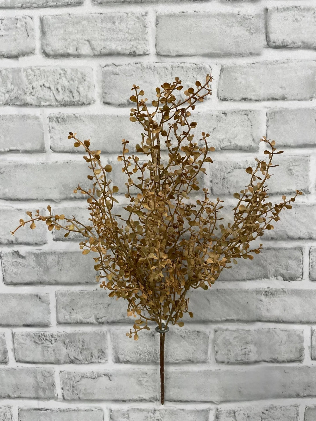 Branche décorative artificielle Maison Olive aux feuilles dorées automnales sur fond de mur en briques grises
