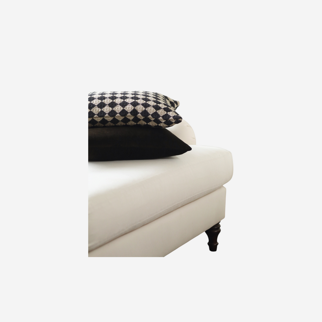 Coussin rectangulaire Maison Olive en velours brun profond superposé à un coussin à motif losanges sur un canapé blanc