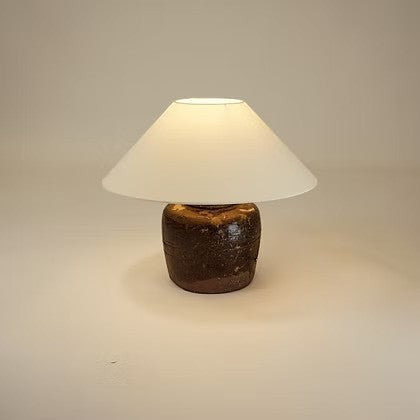 Lampe de table Maison Olive artisanale avec base en terre cuite brune texturée et abat-jour conique en tissu blanc.