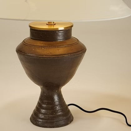 Lampe de table Maison Olive en céramique sombre texturée avec détails en laiton doré et abat-jour en tissu clair.