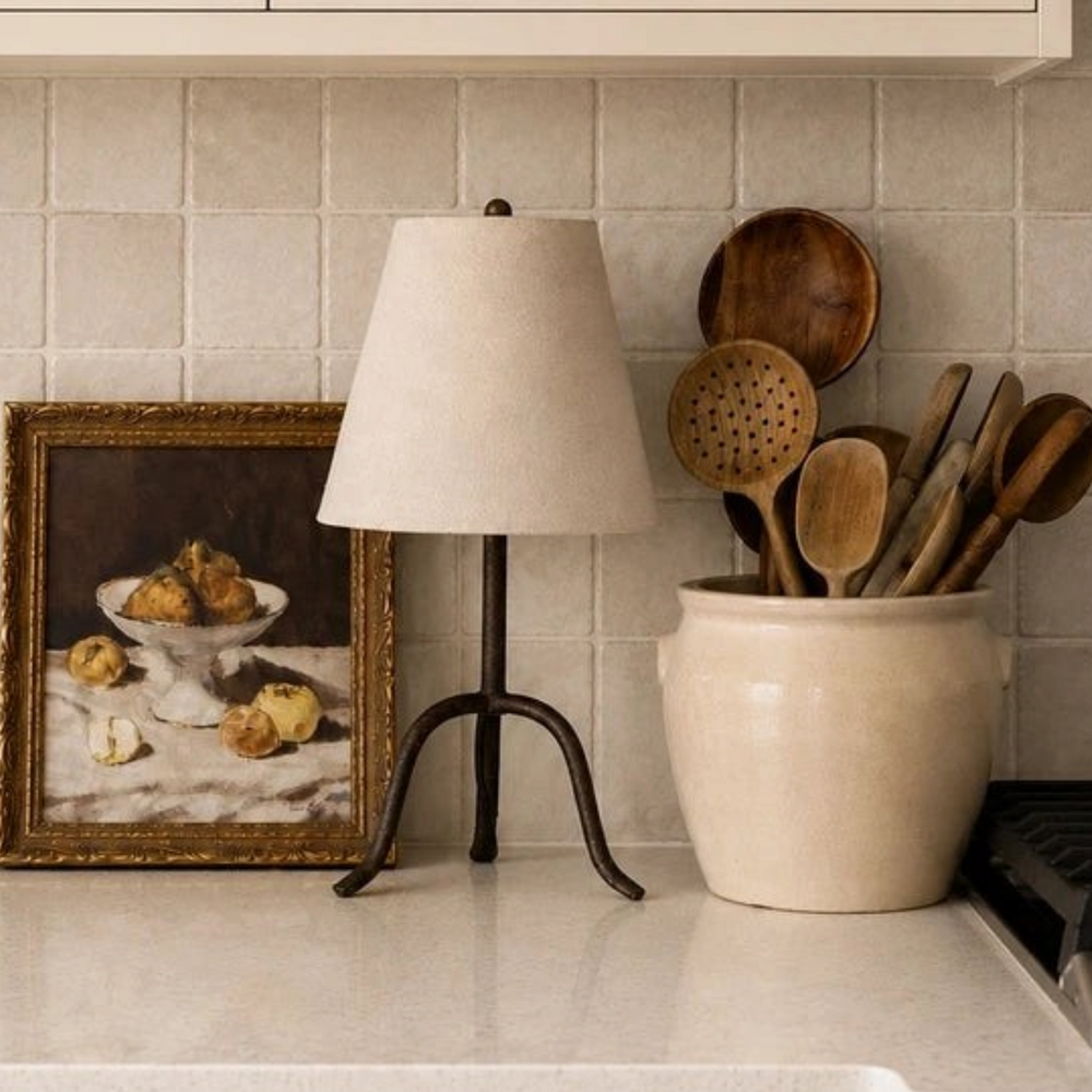 Lampe de table Maison Olive Collins avec abat-jour en lin beige et base trépied en fer forgé sur un comptoir de cuisine
