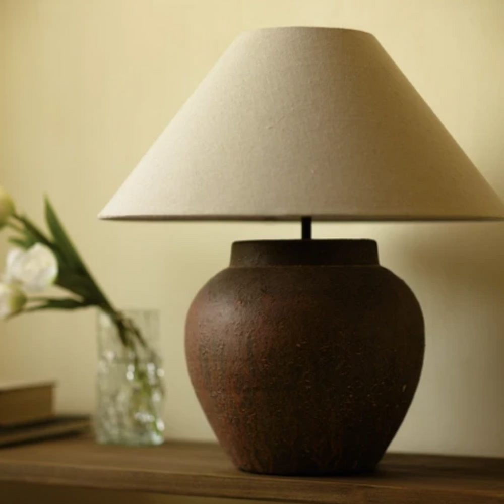 Lampe de table Maison Olive en terre cuite brune texturée avec un abat-jour en tissu beige sur une console en bois.