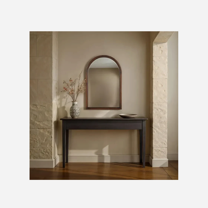Miroir mural arqué Maison Olive avec cadre en bois finition noyer, suspendu au-dessus d'une console dans une entrée.