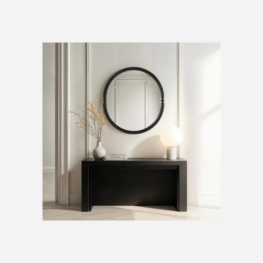 Miroir ovale Maison Olive avec cadre en fer noir mat et détails perlés, posé au-dessus d'une console moderne.