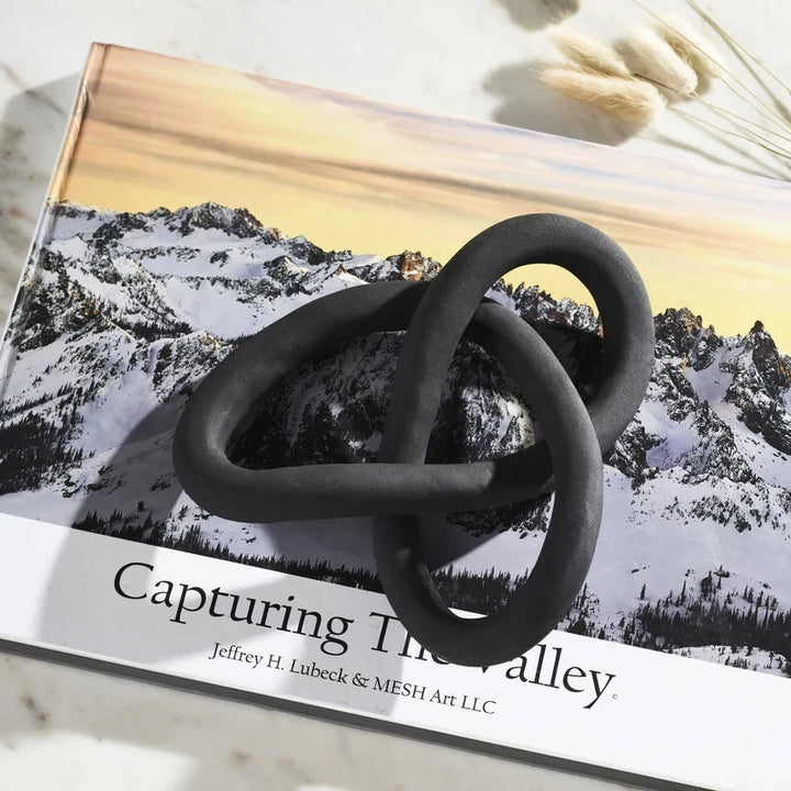 Objet décoratif Maison Olive en forme de nœud sculptural noir mat posé sur un livre de photographie de montagne