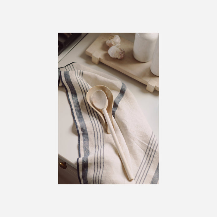 Repose-cuillère Maison Olive en céramique couleur sable posé sur un torchon rayé avec une cuillère en bois