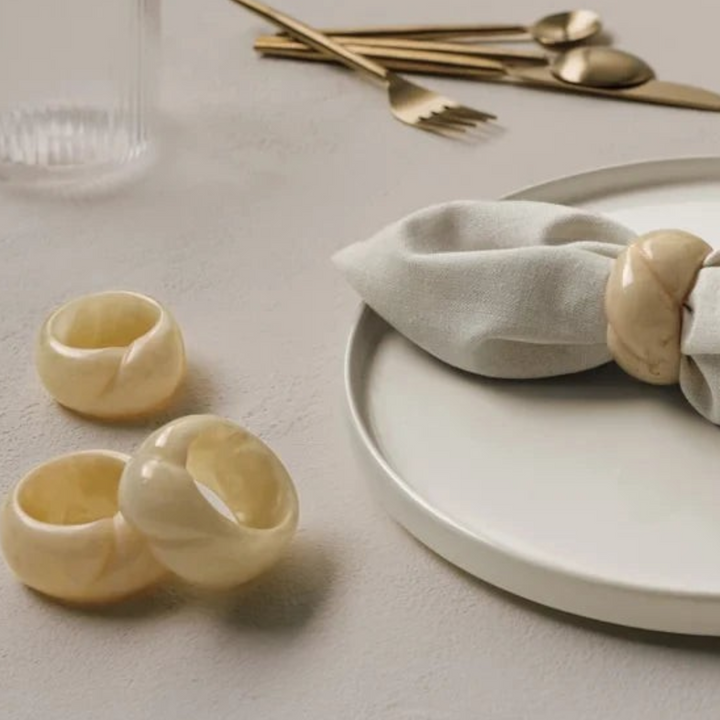 Ensemble de quatre ronds de serviette Maison Olive en résine beige effet pierre polie sur une table élégante