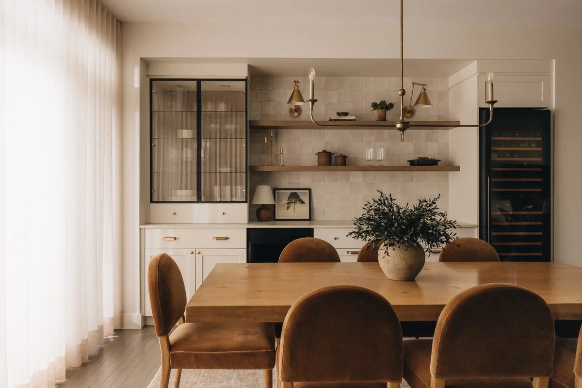Salle à manger lumineuse avec table en bois, chaises brunes et vase de feuillage