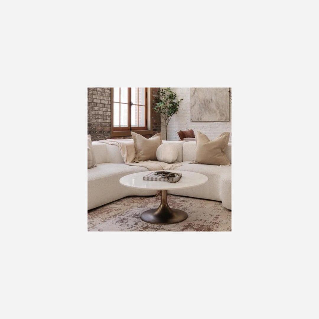 Table basse Maison Olive Lavisa avec plateau en marbre blanc rond et pied central en laiton antique devant un canapé