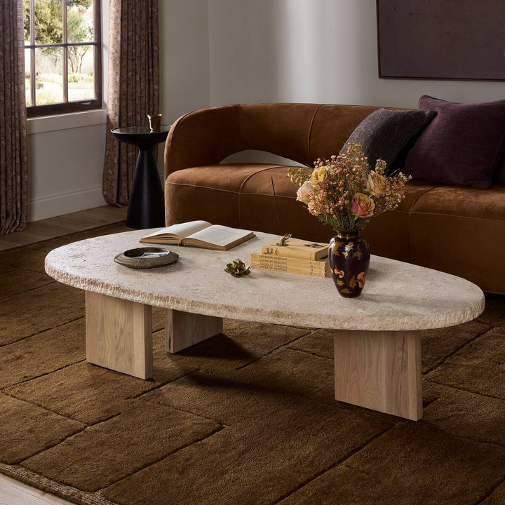 Maison Olive table basse ovale en travertin beige texturé avec pieds en bois clair. Style naturel et chaleureux.