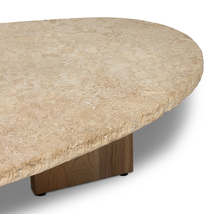 Table basse Maison Olive en travertin beige texturé aux bords bruts, avec un pied en bois massif.