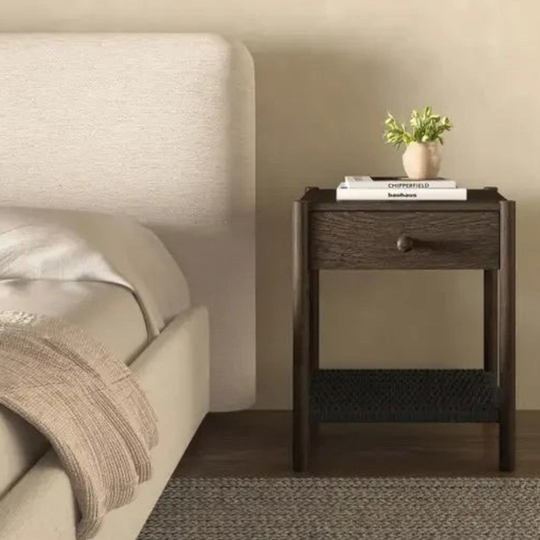 Table de chevet Maison Olive en bois foncé avec tiroir et étagère en corde tressée noire près d'un lit beige