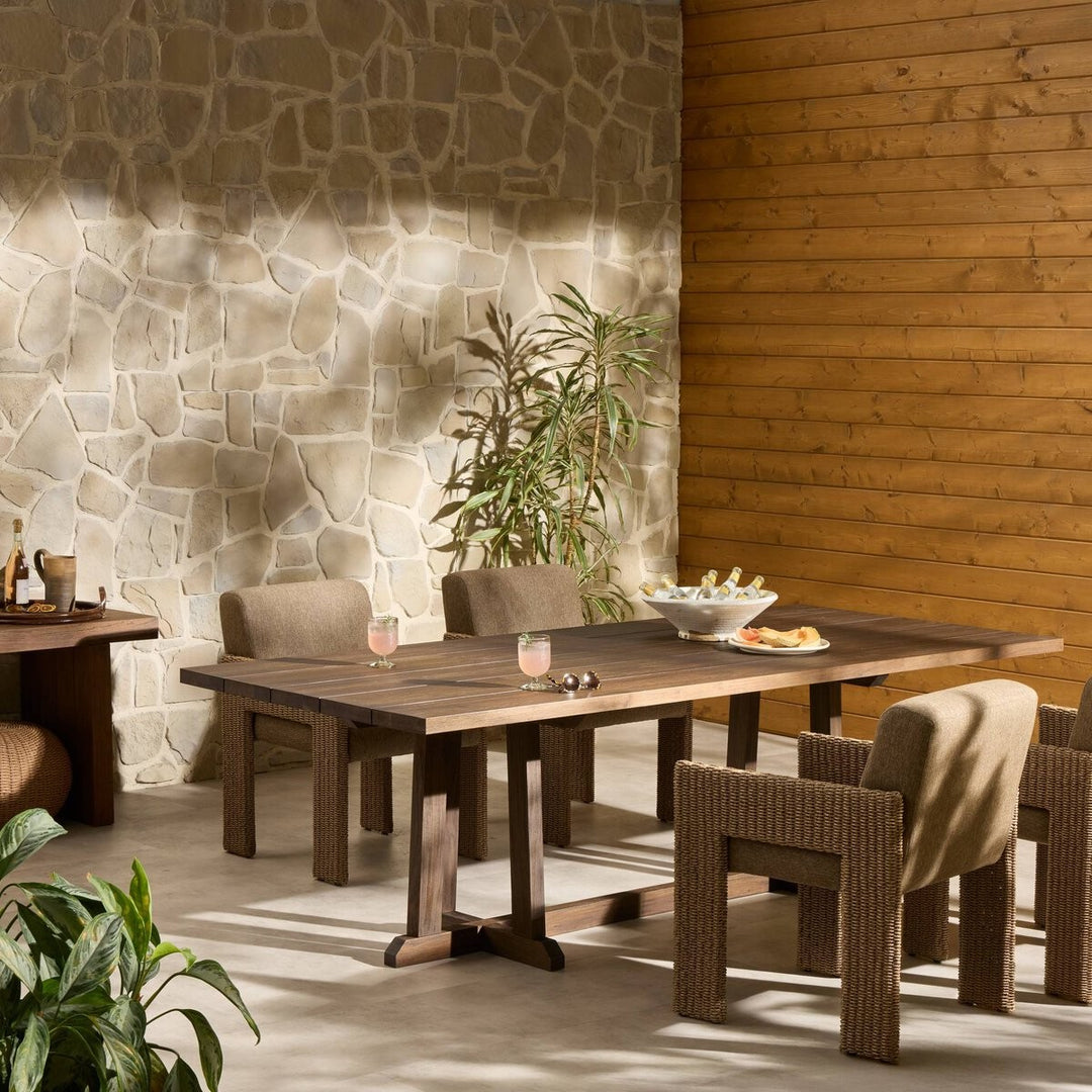 Maison Olive table à manger d'extérieur en bois de teck avec pieds croisés, plateau à lattes et finition naturelle.
