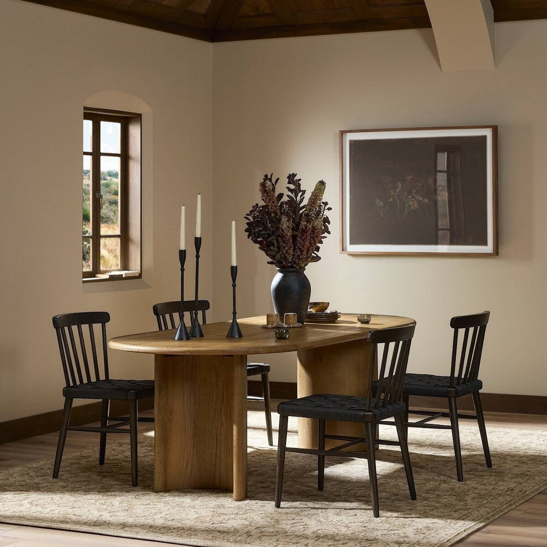 Maison Olive Table à manger ovale en bois d'acacia noir vieilli avec piétement cylindrique et 4 chaises noires.
