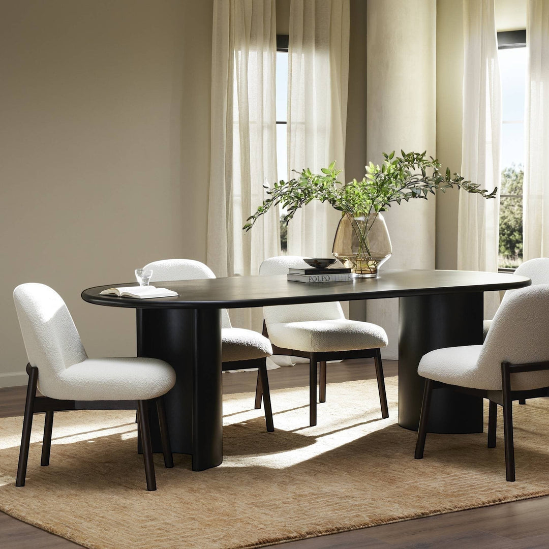 Table à manger ovale en bois noir Maison Olive avec piétement cylindrique, chaises bouclette blanches assorties.