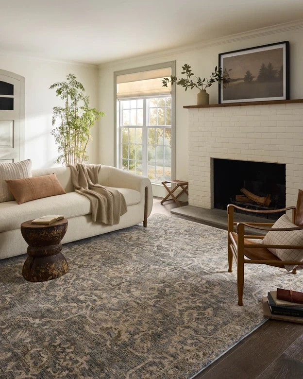 Tapis Maison Olive Junie bleu et naturel au motif antique dans un salon lumineux avec canapé beige et cheminée