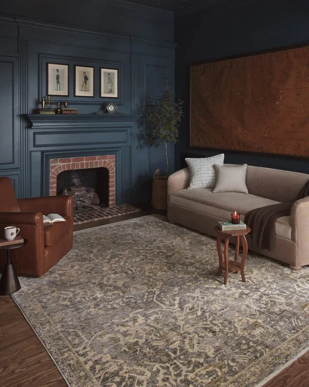 Tapis Maison Olive Junie bleu et naturel à motifs antiques dans un salon élégant avec cheminée et canapé beige
