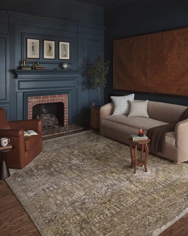 Tapis Maison Olive Junie aux tons mousse et naturel, motif antique vieilli, posé dans un salon élégant.